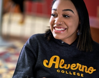 A student wearing an Alverno sweatshirt smiles